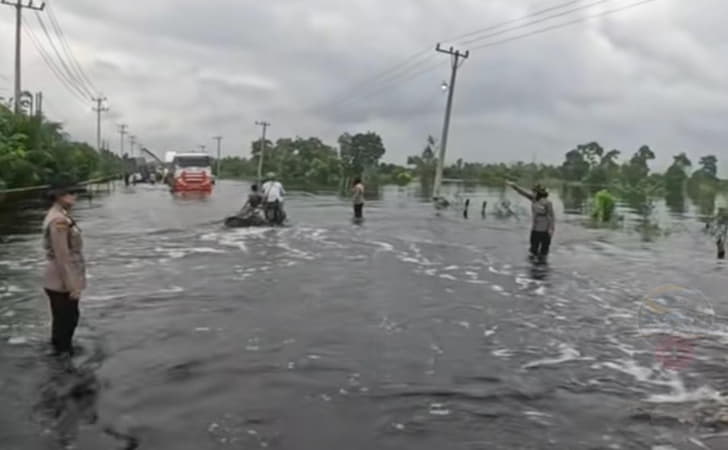 Dua Polwan personel Polres Pelalawan mengatur arus lalu lintas di Jalintim KM 83 yang digenangi banjir.